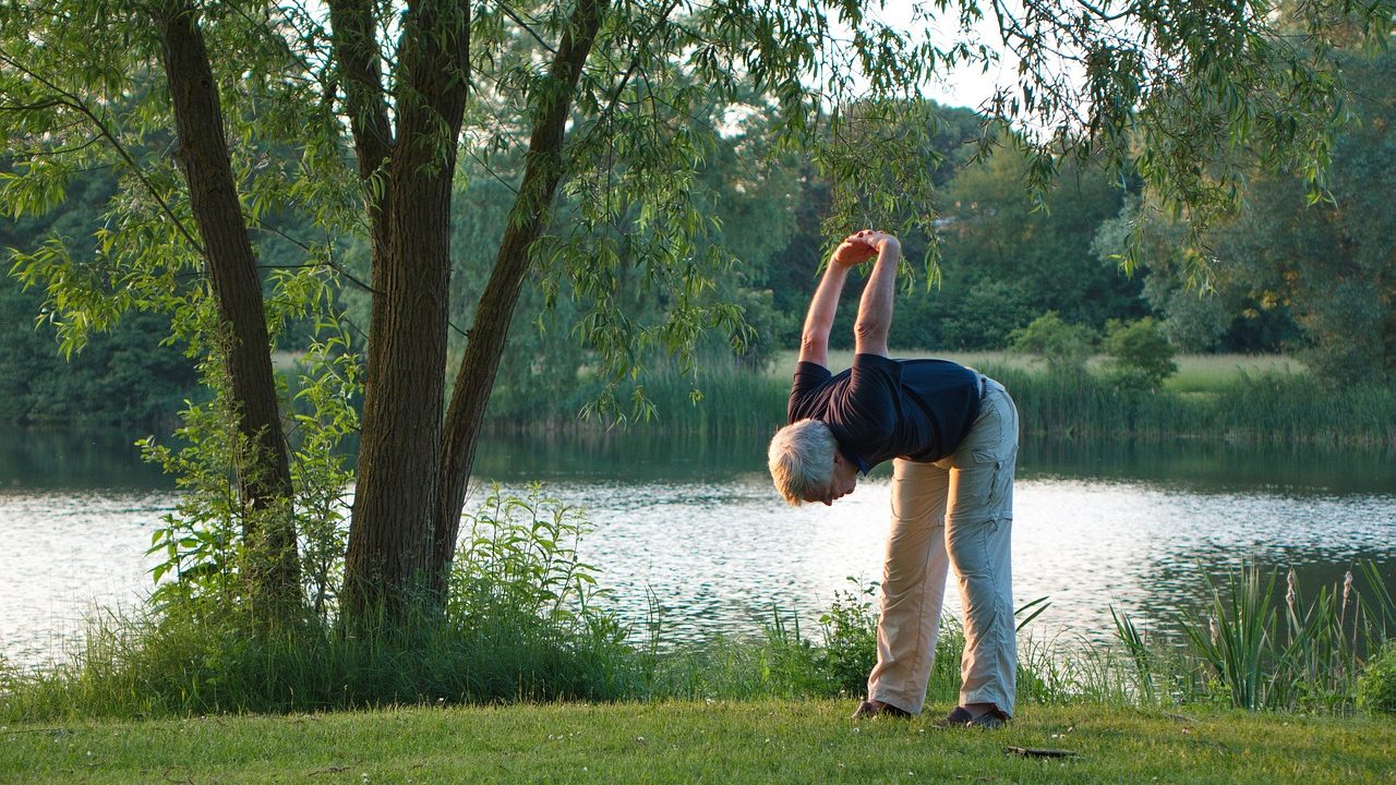 Un senior qui pratique le yoga en pleine nature, près d'un lac