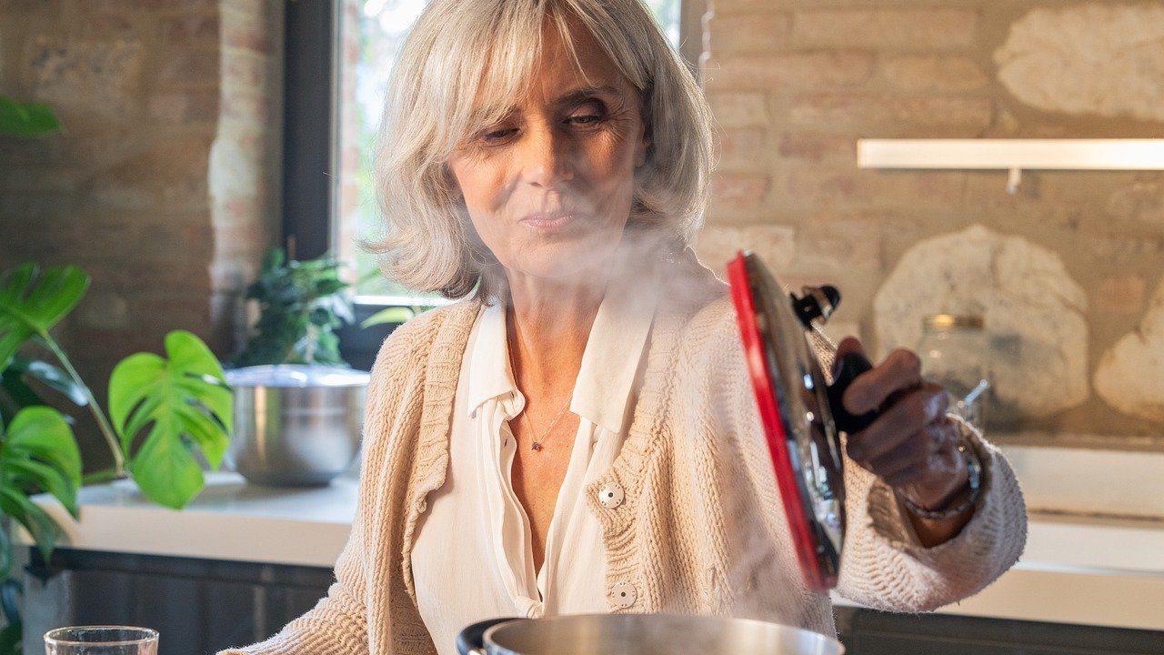 Une femme senior qui soulève le couvercle d'une casserole dans sa cuisine