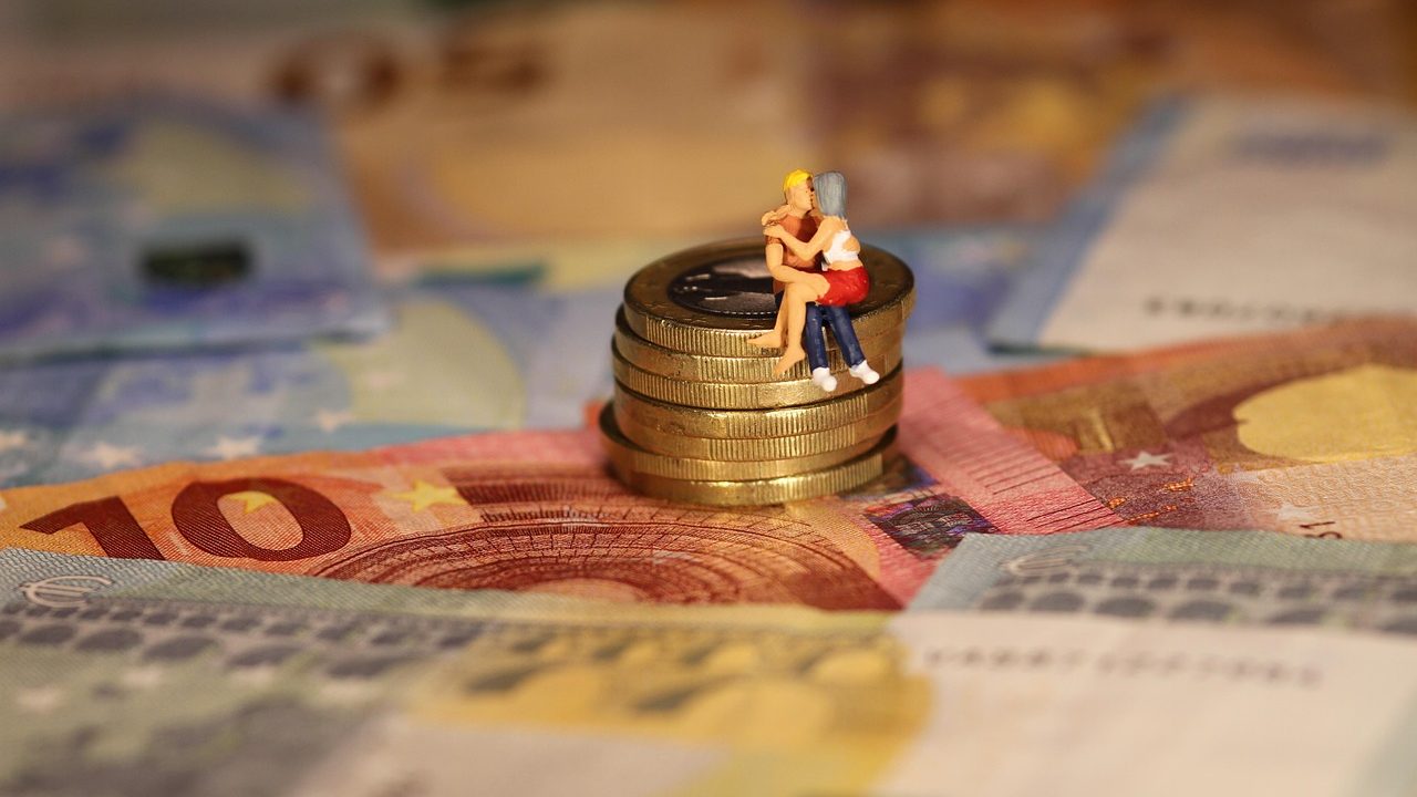 Figurines d'un couple posées sur un tas de pièces et de billets